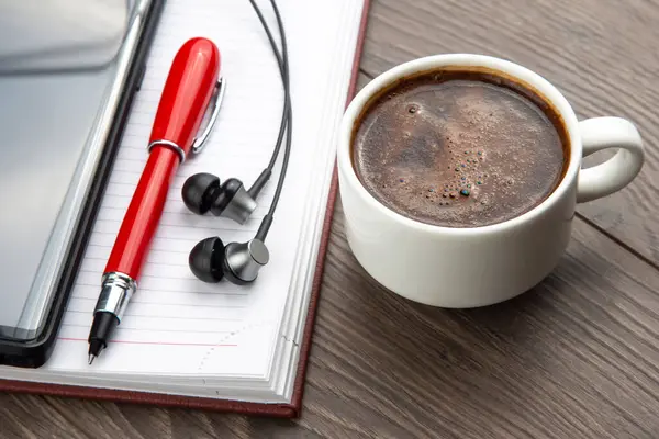 cup of black coffee,  pen,  mobile phone,  notebook and headphones are on the table. Business office items.