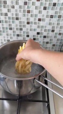 İsimsiz biri, tagliatelle 'i kaynar suyun içine koymuş. Mutfakta yemek ve yemek. Sağlıklı beslenme. - Evet. Yüksek kalite 4k görüntü