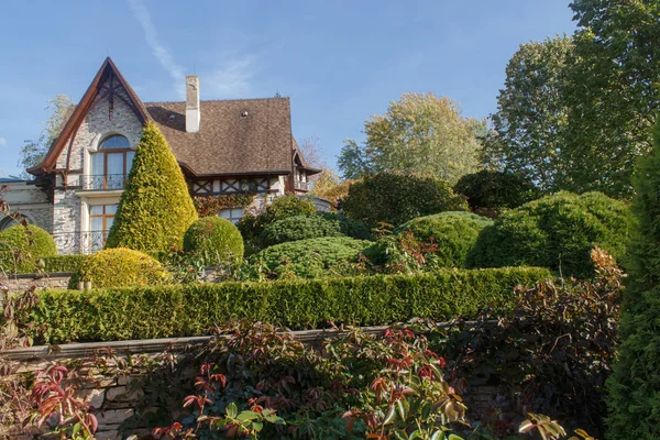 Cottage garden with vines, trees and trimmed bushes.