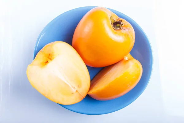 Ώριμα πορτοκαλί Περσίμον σε μπλε πιάτο απομονωμένα σε λευκό προγρό — Φωτογραφία Αρχείου