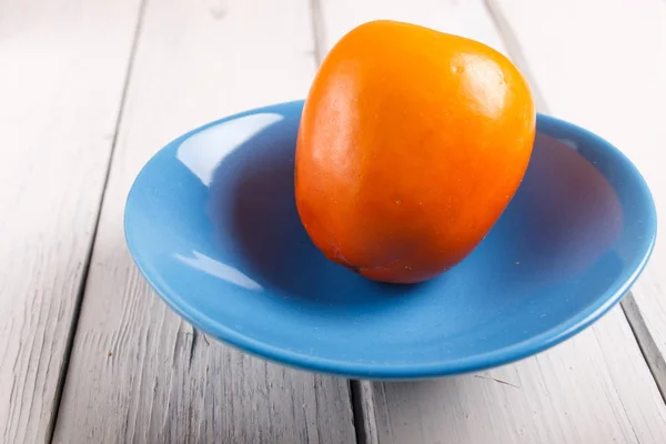 흰색 나무 배경에 파란색 접시에 잘 익은 오렌지 감 — 스톡 사진