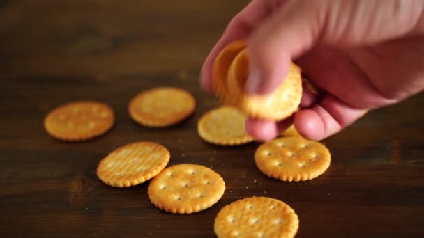 Un bisküvisi tuzlu kraker ahşap bir arka planda duruyor. İnsan eli birini alır. — Stok video