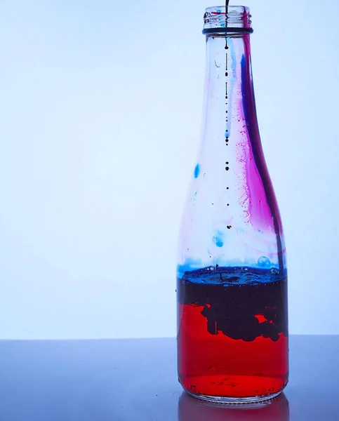 青いインクは赤い液体の入ったガラス瓶の中に落ちます 混合効果 高品質の写真 — ストック写真
