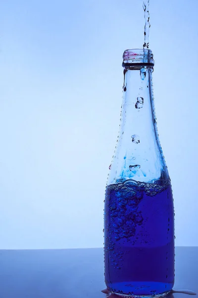 Een blauwe vloeistof wordt in een glazen fles gegoten. Lichtblauwe achtergrond — Stockfoto