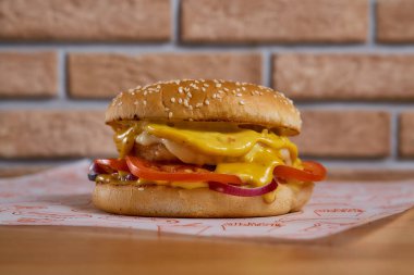 Tahta bir masada soğanlı, salatalıklı, marullu, peynirli sulu burger. tuğla arka plan. Yüksek kalite fotoğraf
