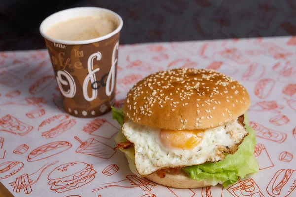 Burger with egg, bacon and lettuce on a light background with takeaway coffee . High quality photo