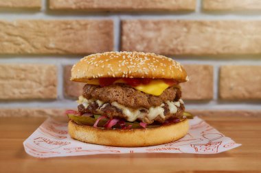 Tahta bir masada soğanlı, salatalıklı, marullu, peynirli sulu burger. tuğla arka plan. Yüksek kalite fotoğraf