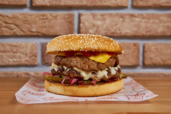 Tahta bir masada soğanlı, salatalıklı, marullu, peynirli sulu burger. tuğla arka plan. Yüksek kalite fotoğraf