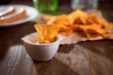 Tahta bir masanın üzerinde Meksika mısır cipsi var. Soslu bir kasede tek bir şey. Yüksek kalite fotoğraf