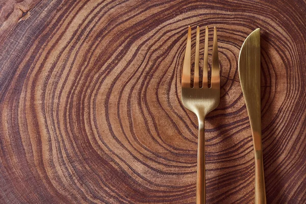 El tenedor de oro y el cuchillo se encuentran en una rebanada de un árbol. Mesa de madera. Con espacio de copia . — Foto de Stock