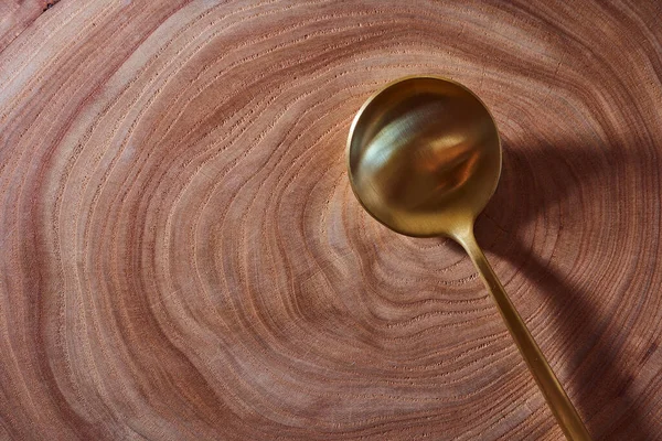 La cuchara dorada yace en una rebanada de un árbol. Mesa de madera. Con espacio de copia . — Foto de Stock