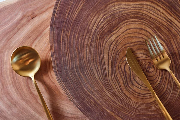 La cuchara de oro, el cuchillo y el tenedor se encuentran en una rebanada de un árbol. Mesa de madera. Con espacio de copia . — Foto de Stock