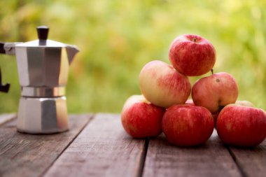 Gayzer kahve makinesi, yeşil bulanık arka plana karşı tahta bir tahtanın üzerinde duruyor. Kırmızı elmalarla. Kopyalama alanı olan. Yüksek kalite fotoğraf