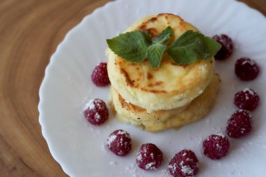 Meyveli peynirli kekler beyaz bir çay tabağının üzerinde ahududu ve nane yaprağı ile yatar. Hafif arkaplan. Yüksek kalite fotoğraf