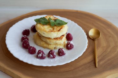 Meyveli peynirli kekler beyaz bir çay tabağının üzerinde ahududu ve nane yaprağı ile yatar. Hafif arkaplan. Yüksek kalite fotoğraf