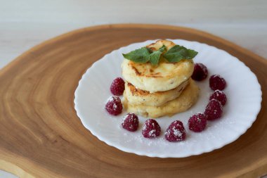 Meyveli peynirli kekler beyaz bir çay tabağının üzerinde ahududu ve nane yaprağı ile yatar. Hafif arkaplan. Yüksek kalite fotoğraf