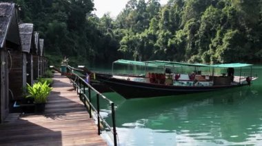 Göl kenarında sazdan çatı evi. iskeleye bağlı tekne dalgaların üzerinde Bobs, Cheow lan Gölü. Khao Sok Milli Parkı. Tayland.