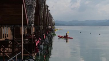 Sazdan çatılı bir gölde duran birkaç bungalov. İnsanlar kanoyla yüzüyor. Kayaklar iskeleye park ettiler. Cheow lan Gölü. Khao Sok Tayland.