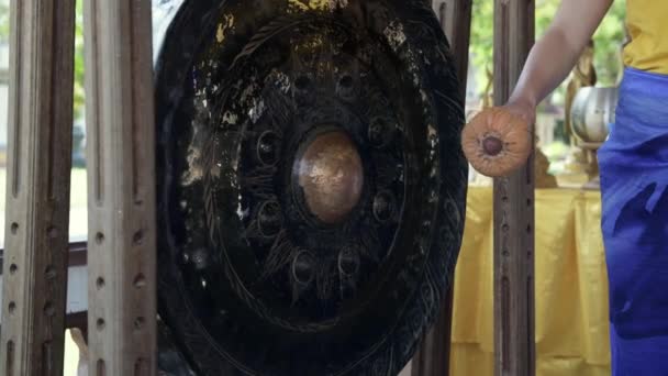 Person hand striking small Asian gong close up. Static shot of miniature gong in focus with shallow depth of field. Placed on wooden desk. Female hand — Stock Video