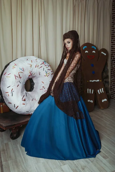 Model wearing historical dress is posing in a studio with a giant donut