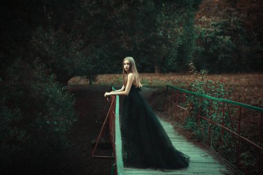 Karanlık bir ormanda siyah elbise giyen genç kız poz
