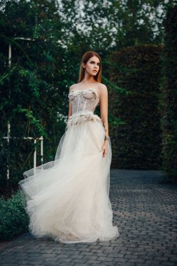Genç güzel model bir taç kafasındaki ile bahçedeki uzun Fildişi elbiseyle poz 