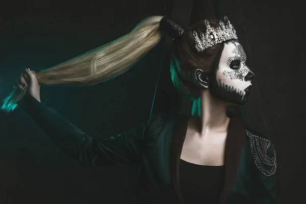 Beautiful model is posing in a dark studio with a skull on her face