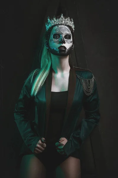 Beautiful model is posing in a dark studio with a skull on her face