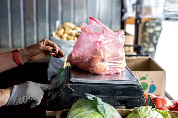 O vendedor de legumes no mercado está pesando mercadorias em balanças para um comprador Imagem De Stock