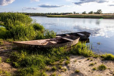 Tekne yeşil bir çimenlikte, gölün kıyısına demirlemiş.
