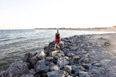 Bir adam deniz kenarındaki taşların üzerinde duruyor. Yaz yerel turizmi