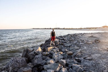 Bir adam deniz kenarındaki taşların üzerinde duruyor. Yaz yerel turizmi