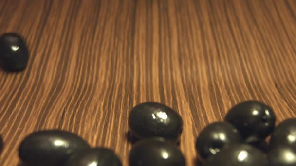 Olives noires sur fond de bois brun. 2 coups de feu. Au ralenti. Gros plan 1. Olives roulent vers le bas sur un fond en bois marron.2. Panneau horizontal (de gauche à droite) . 