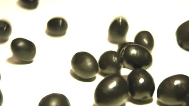 Olives noires sur fond blanc. 2 coups de feu. Au ralenti. Gros plan 1. Les olives roulent sur un fond blanc.2. Panneau horizontal (de droite à gauche) . 