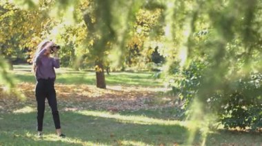 Park kız. Fotoğraf makinesi Park ile kız duruyor. O doğa fotoğraf çeker ve çerçeve dikkatle inşa ediyor. Parlar güneş rüzgar. (Sağdan sola) yatay pan.