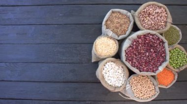 Baklagiller koyu ahşap ekolojik arka plan üzerinde. Fasulye siyah ahşap masa üzerinde daire şeklinde yer alır. Fasulye kültürlerde örme çanta. Kamera soldan sağa taşır.. 