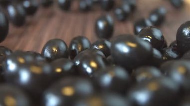 Siyah Zeytin kahverengi ahşap zemin üzerinde. 2 Shots.Slow hareket. Yakın-up.1. zeytin kahverengi ahşap arka plan üzerinde aşağı yuvarlanan ve tüm alanı frame.2 doldurun. Dikey (yukarıdan aşağıya) pan.