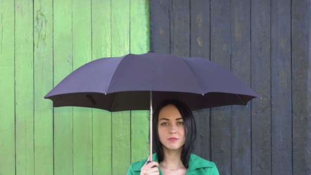 大雨倾盆而下 女孩躲在伞下 女孩把头发放在伞下 然后开始下雨 它加强 过了一会儿雨停了 女孩在彩色背景看着相机没有情感 — 图库视频影像
