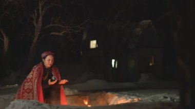 Şenlik ateşinin yanında bir kız. Kız ellerini ısıtır ve battaniyenin altında ateşin yanında gülümser. Kıvılcımlar birbirinden ayrı uçar. O sıcak giysiler giymiş. Arka bahçede geceleri rahatlayın. House arka planda duruyor. Kış.