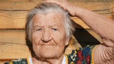 Büyükannem saçını şekillendiriyor. Yaşlı kadının buruşuk yüzü. Ahşap rustik arka plan üzerinde Büyükanne onu gri saç dokunur ve yavaşça geri koyar. Yaşlı büyükanne kameraya bakıyor. 91 yaşındaki büyükanne.