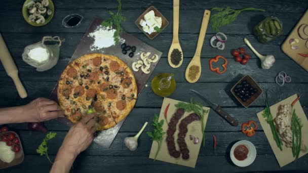 Pizza on ecological black background.Man cuts a piece of pizza and give it to girl. Meat pizza with different filling: salami, mushrooms, sausage, cheese, olives. There are also many other products on table for cooking and eating pizza.