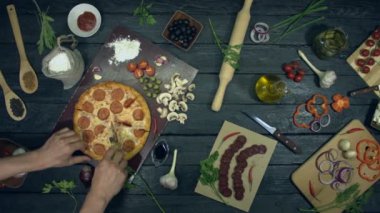 Ekolojik siyah arka planda Pepperoni pizza. Adam bir parça biberli pizza keser ve ona götürür. Dolgulu pizza: salam, farklı peynir. Yemek pişirmek ve pizza yemek için masada birçok ürün de vardır.