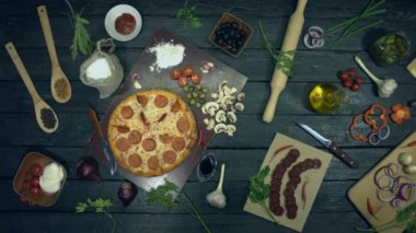 Ekolojik siyah arka planda Pepperoni pizza. Stop Motion.Pizza masada kendi kendine dönüyor. Dolgulu pizza: salam, farklı peynir. Yemek pişirmek ve pizza yemek için masada birçok ürün de vardır.