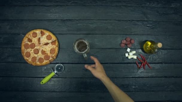 エコロジカルな黒の背景にビールとペパロニピザ 男はテーブルからビールとピザを取る 充填ピザ サラミ 異なるチーズ モッツァレラ 唐辛子 ソーセージ ヒマワリ油の材料があります — ストック動画