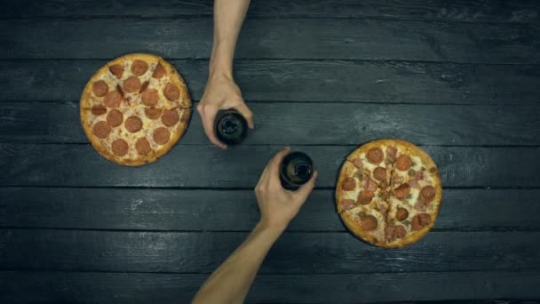 生態学的な黒い背景にベジタリアンピザ 男は瓶からグラスにビールを注ぐ 異なる充填とピザ トマト ピーマン キノコ 様々なチーズ オリーブ ピザを食べるためのテーブルの上に他の多くの製品があります — ストック動画