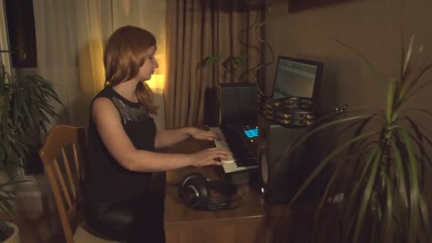 家庭录音室 一个年轻女子在中音键盘上玩 摄像机从左向右移动 显示器屏幕关闭 — 图库视频影像