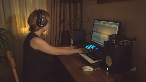 ホームレコーディングスタジオ ある若い女性がコンピュータのMidiキーボードを使って音楽を書きます そして 彼女は記録された結果に耳を傾ける — ストック動画