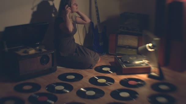 その少女は古いラジオを聞く 2ショット その少女は床に座っている 彼女の隣には古いレコード ターンテーブル リールテープレコーダー ラジオ ギターがあります 彼女はヘッドフォンをつけてラジオ2をオンにします ラジオクローズアップ — ストック動画