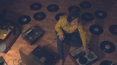 Kız müzik çoğaltma ve ses kayıt için vintage cihazlar ile çevrili dinler. Kız yerde oturuyor. Onun yanında 60'lı, 70'li ve 80'li yaşların bobin bant kayıt cihazları, eski bir pikap ve kayıtlar. Bandı düzeltir..