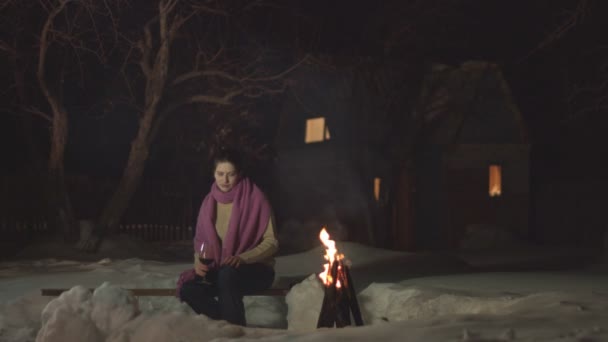 女孩喝红色水果饮料 女孩看着火 喝红色水果饮料 屋后的雪冬 — 图库视频影像
